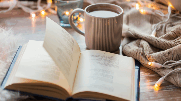 An open book resting on a table with a cup of tea, symbolizing relaxation, rest, and intentional wellness